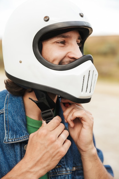 Close up of a young man wearing casual outfit at the beach, putting on a helmet