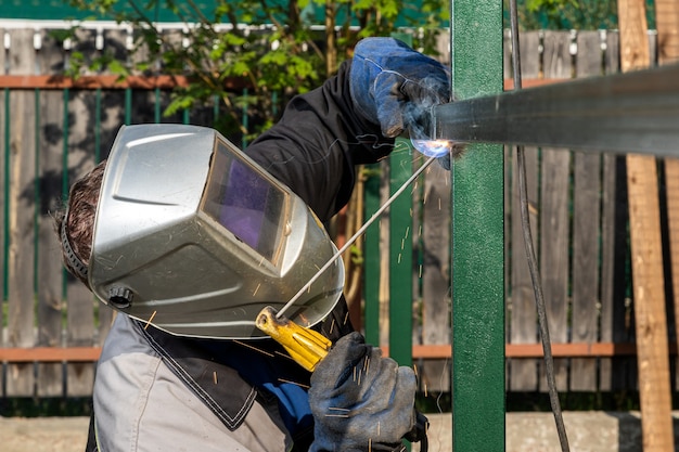 close up of a young  man welder in  uniform, welding mask and welders leathers, weld  metal  