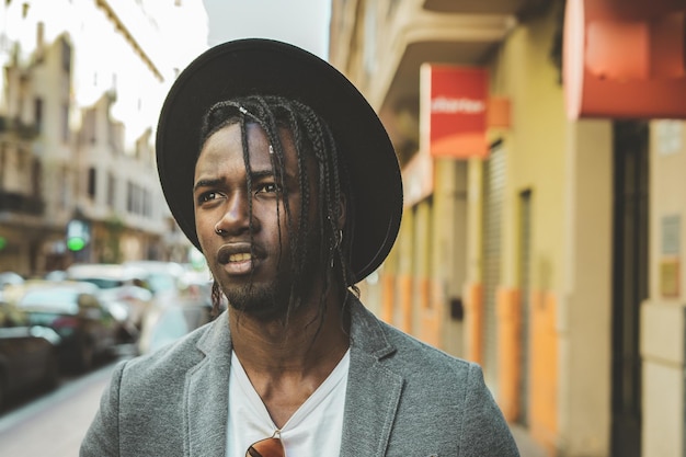 Close-up of young man with braided hair wearing hat in city