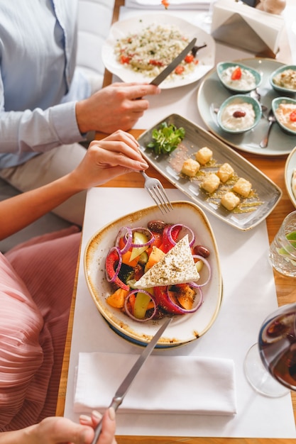 Close up of young man and woman sitting at the table with fresh salads and sauces