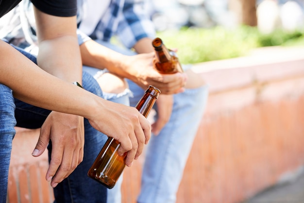 Close-up of young men holding bottles of beer while sitting outdoors