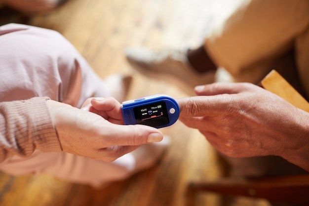 Photo close up of young nurse putting oximeter of finger of senior woman, copy space