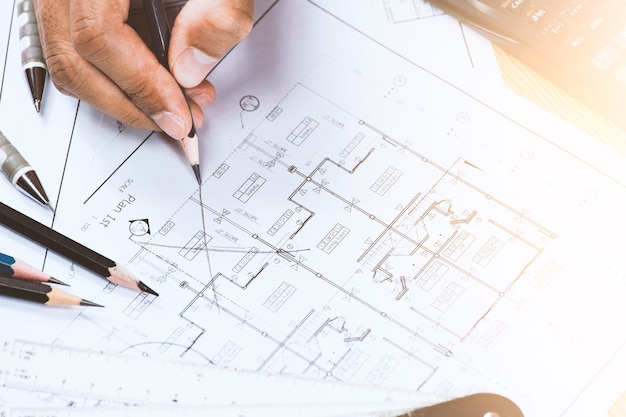 Close-up of young person hands marking on blue print with architect instrument at office desk.