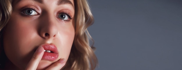 Close-up young pretty blonde woman with finger at lips flirts look against dark blue insulation background. Female emotion happy and actress of master. Concept of satisfaction inspiration. Copy space