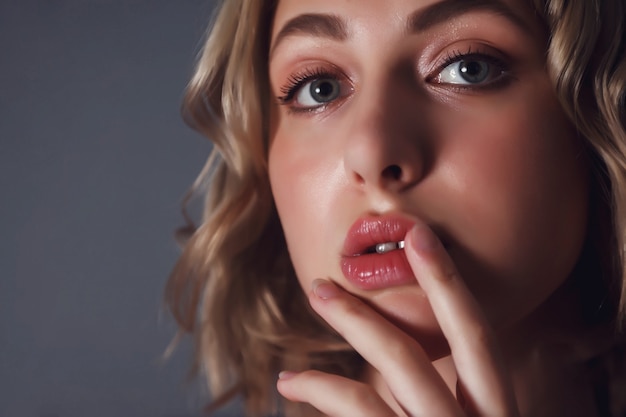 Photo close-up young pretty blonde woman with finger at lips flirts look