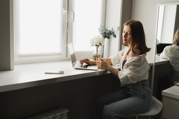 Close up of young pretty concentrated woman typing and browsing online on laptop working on computer