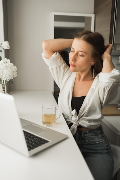 Close up of young pretty woman drinking tea while break after typing and browsing online on laptop w