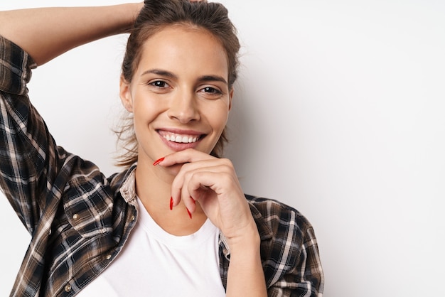 Close up of a young smiling beautiful girl wearing plaid shirt standing isolated over white wall, posing
