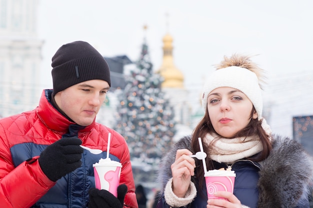 Закройте молодых возлюбленных в куртках, держа молочный коктейль в зимний сезон на открытом воздухе.