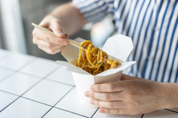 Close-up of a young unidentified man's hand in a shirt are holding wooden sticks chinese noodle