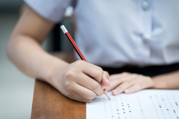 Primo piano di giovani studenti universitari si concentrano sul fare l'esame in classe. la studentessa scrive sulla carta di risposta agli esami in classe.