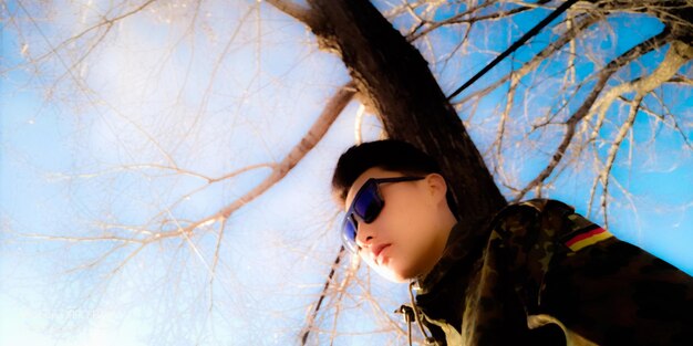 Close-up of young woman against bare tree against clear blue sky