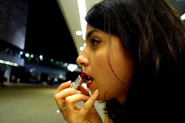 Close-up of young woman applying lipstick at night