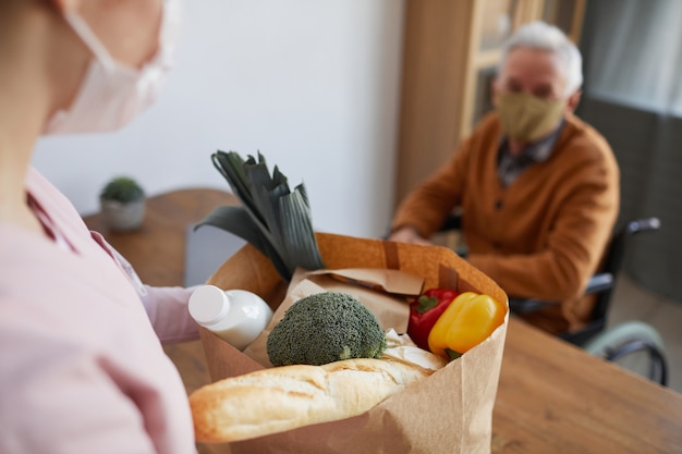 Foto primo piano di una giovane donna che porta la spesa all'uomo anziano in sedia a rotelle, concetto di servizio di consegna cibo, spazio copia