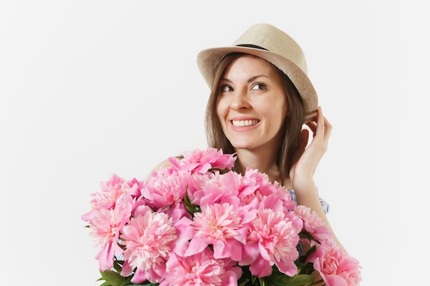 Primo piano di una giovane donna in abito, cappello che tiene il mazzo di bellissimi fiori di peonie rosa isolati su sfondo bianco. san valentino, concetto di vacanza per la giornata internazionale della donna. zona pubblicità.