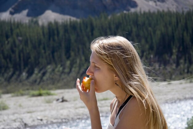 Foto close-up di una giovane donna che mangia pesche contro gli alberi nel parco nazionale di banff