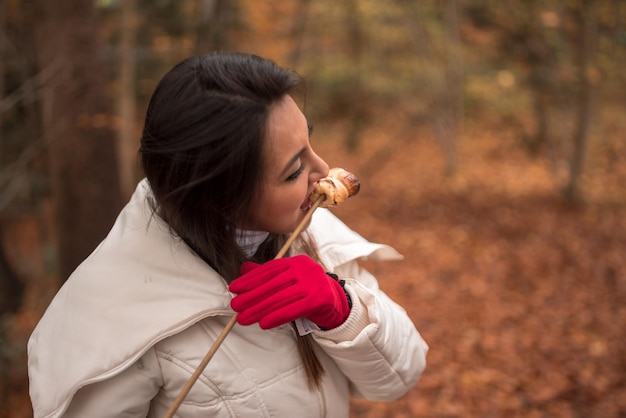 Photo close-up of young woman eating roasted marshmallow in forest
