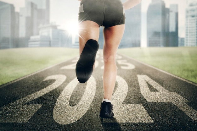 Close up of young woman foot running and exercising on the track with 2024 new year numbers and cityscape background