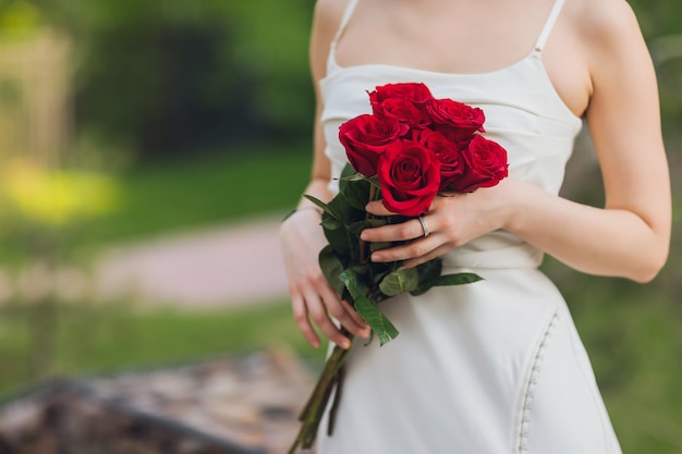 屋外の背景に赤いバラの花を持っている若い女性の手のクローズアップ。