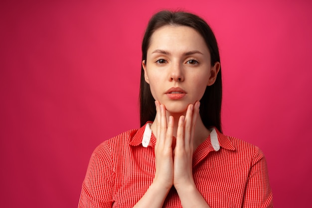 Close up of a young woman holding face in hands against pink background