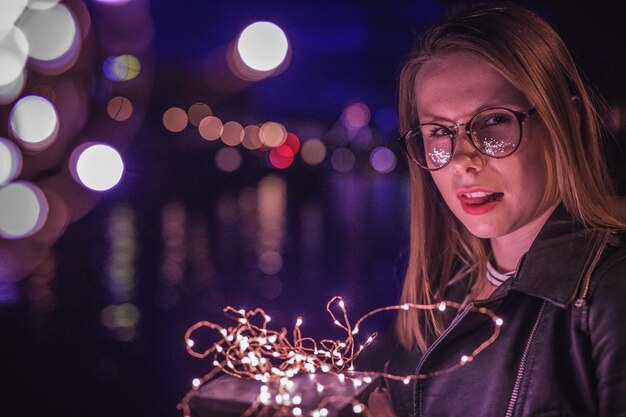 Фото Клоуз-ап молодой женщины с освещенной струнной лампой ночью