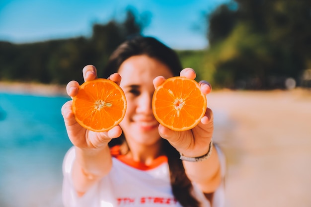 Close-up of young woman holding orange at beach