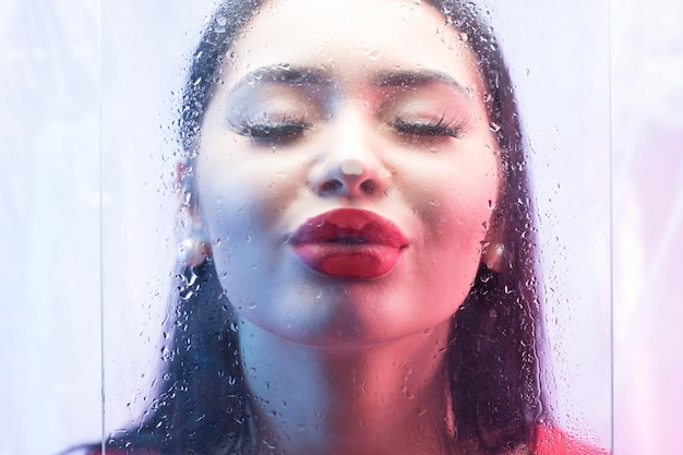 Photo close-up of young woman kissing wet glass