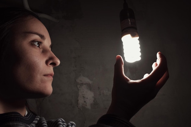 Foto close-up di una giovane donna che guarda una lampadina illuminata