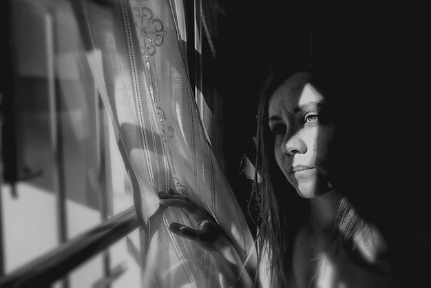 close-up of young woman looking through window at home