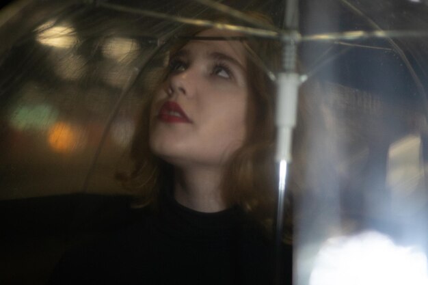 Close-up of young woman looking up through umbrella outdoors