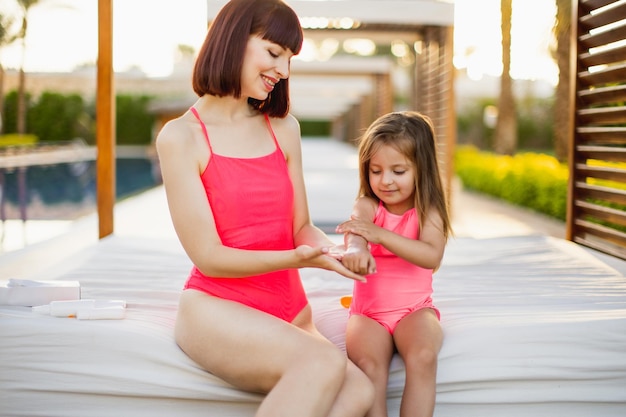 Close up of young woman in a pink swimsuit applying SPF 50 sun protection cream on her daughter