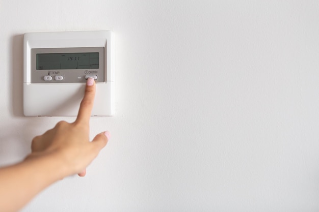 Close-up of a young woman's hand pressing the onoff button of the air conditioner or heater.