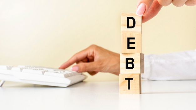 Close up young woman's hand in white shirt wooden block cube for DEBT wording on white table floor, white keyboard on the background. financial and business concepts.