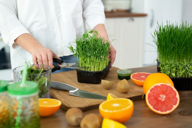 Primo piano delle mani di una giovane donna in cucina che tagliano i micro-piselli verdi pronti per fare un frullato vitaminico.