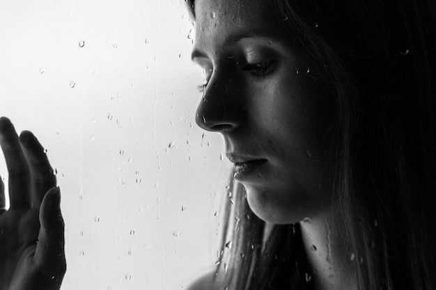 Foto close-up di una giovane donna vista attraverso un vetro bagnato