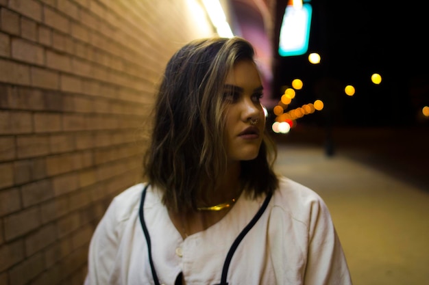 Photo close-up of young woman standing against illuminated wall at night