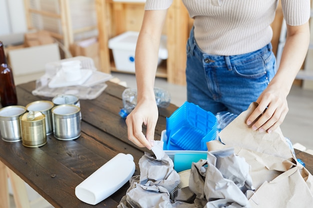 Close-up of young woman standing at the table with waste and sorting it