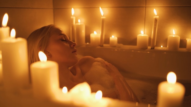 Close up of a young woman taking a bath surrounded by candles