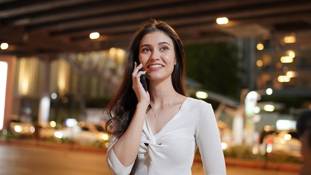 Primo piano giovane donna che parla con qualcuno sul suo telefono cellulare mentre guarda in lontananza con un'espressione facciale felice.