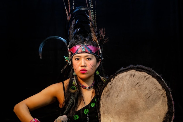Close up of young woman teotihuacana, xicalanca - toltec in\
black background, with traditional dress dance with a trappings\
with feathers and drum