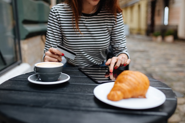 Close up of young woman using digital tablet and a credit card while sitting at cafe table