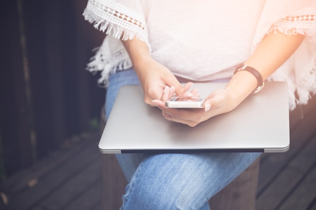 Chiuda sulla giovane donna che per mezzo del telefono cellulare e del computer portatile