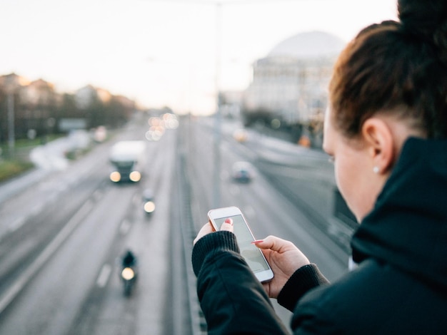 Photo close-up of young woman using smart phone against road in city