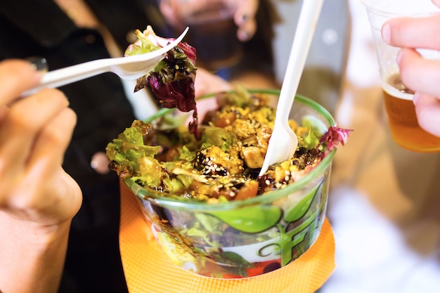 Close-up of young woman visiting eat market and eating colorful salad in the street.