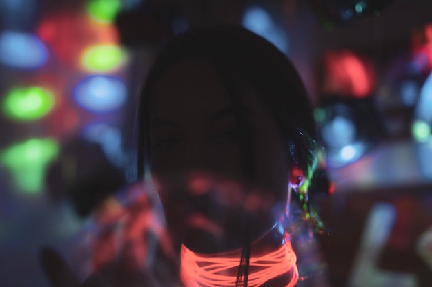 Close-up of young woman wearing illuminated necklace in darkroom