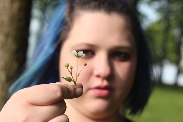 Photo close-up of young woman with blue hair holding flower in park