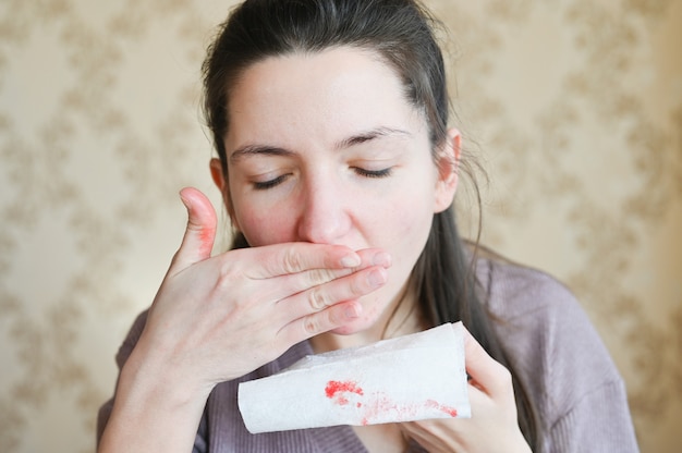 Il primo piano di una giovane donna con paura guarda il sangue sul suo tovagliolo. concetto di persona malata.