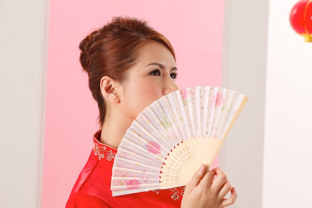 Close-up of young woman with hand fan standing against pink wall