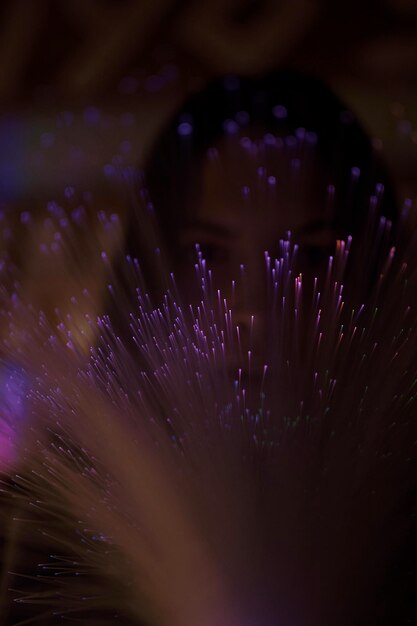 Photo close-up of young woman with illuminated fiber optics in darkroom