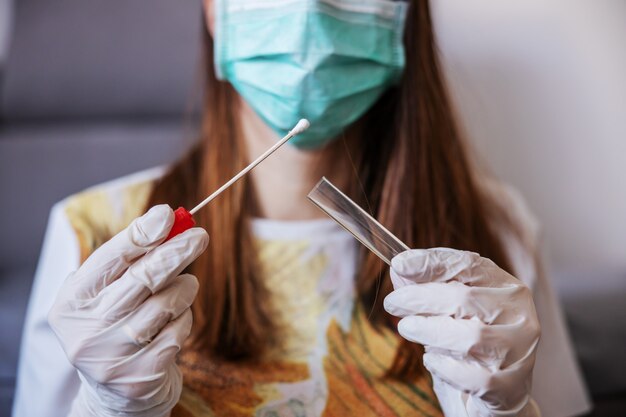 Close up of young woman with sample swab. Selective focus on sample. Corona virus protective measures.